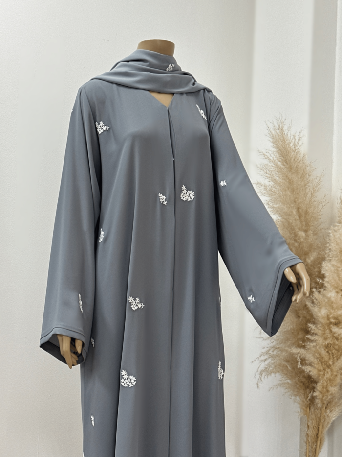 "Front view of an elegant Alishbah Egyptian Crape Abaya, showcasing a graceful silhouette with subtle details. The lightweight fabric drapes beautifully, and a soft chiffon Sheila is styled with it. The model has her hand slightly raised, highlighting the abaya's fluid lines and versatility."