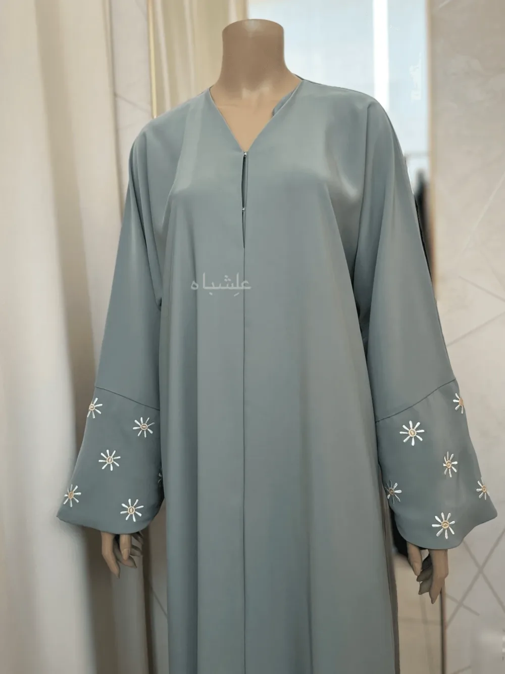 Abaya in green sage featuring premium Nida fabric with delicate floral embroidery on the overlapped sleeves and sheila. The Green Sage Nida Premium Abaya by Alishbah offers a blend of luxury, sophistication, and timeless elegance