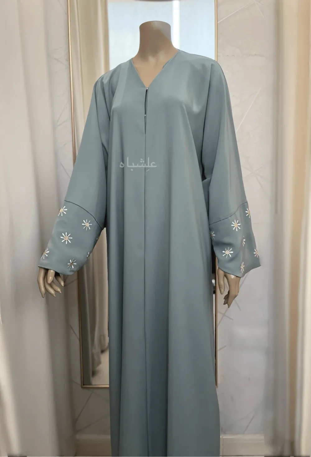 Abaya in green sage featuring premium Nida fabric with delicate floral embroidery on the overlapped sleeves and sheila. The Green Sage Nida Premium Abaya by Alishbah offers a blend of luxury, sophistication, and timeless elegance