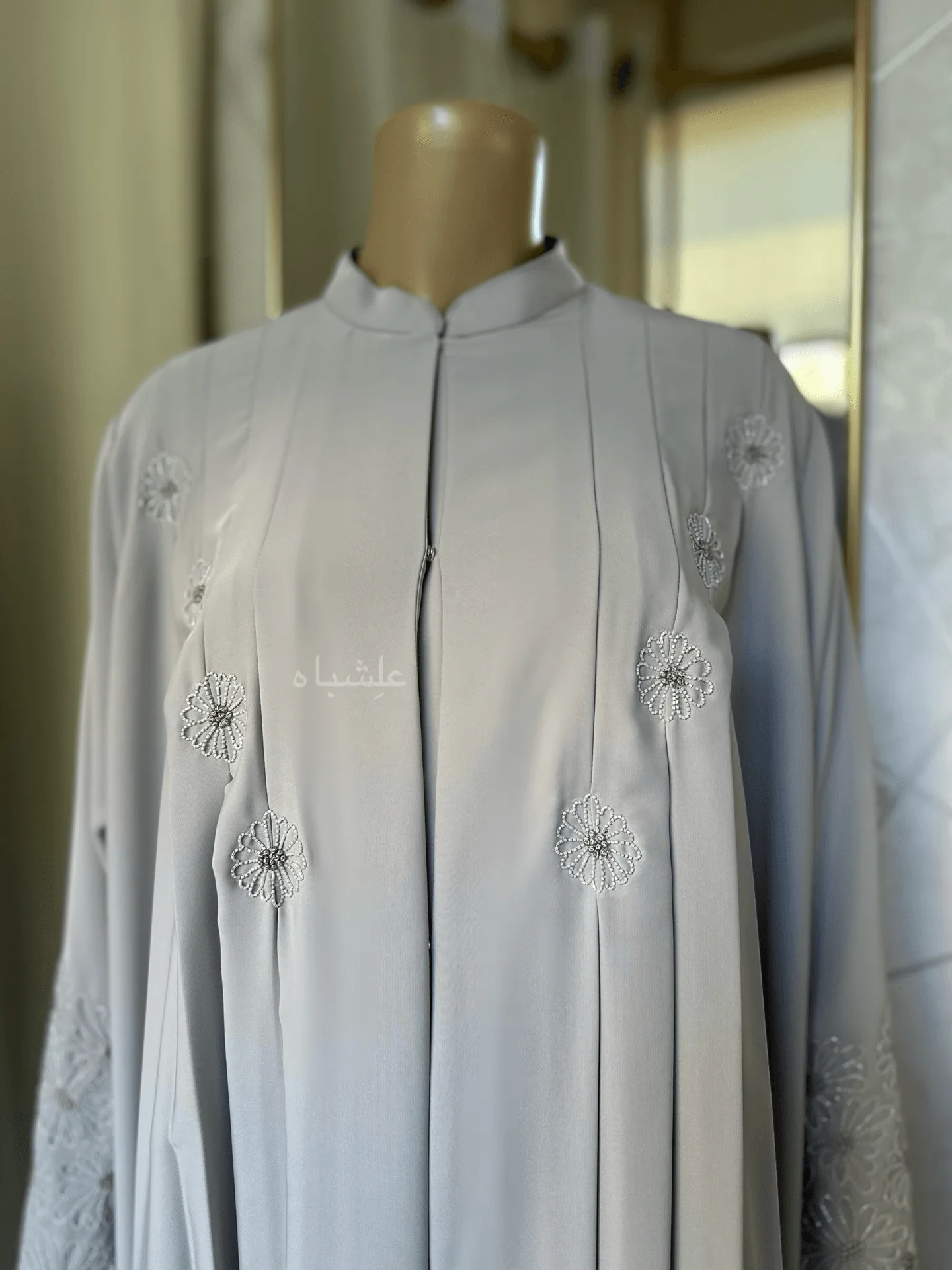 Eternal Petals of Grace Nida Premium Abaya with Floral Handwork 2 Alishbah Eternal Petals of Grace Nida Premium Abaya with floral handwork. The abaya is crafted from luxurious Nida Premium fabric, featuring delicate floral handwork including tiny scallops and French knots that form elegant patterns along the cuffs and neckline. The ensemble is completed with a soft chiffon sheila (headscarf) that drapes gracefully, enhancing the sophisticated and timeless design. This abaya blends traditional handwork with contemporary elegance, showcasing high-quality craftsmanship and refined style.