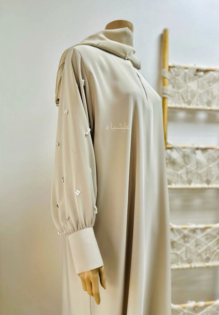 The Cream Nida Premium Fabric Abaya by Alishbah features a luxurious design with intricate embellishments of clip stones, pearls, and tube beads. Made from high-quality Nida fabric, the abaya drapes elegantly with a loose silhouette, ideal for both formal and casual occasions. Its neutral cream color allows for versatile styling, blending tradition with modern sophistication.