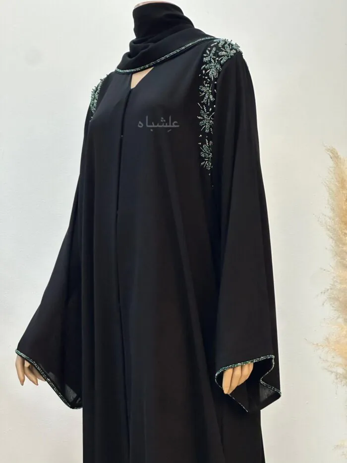 "Black chiffon abaya adorned with intricate sea green beadwork in floral patterns on the shoulders and sleeve ends, draped elegantly on a mannequin with a matching soft chiffon sheila."