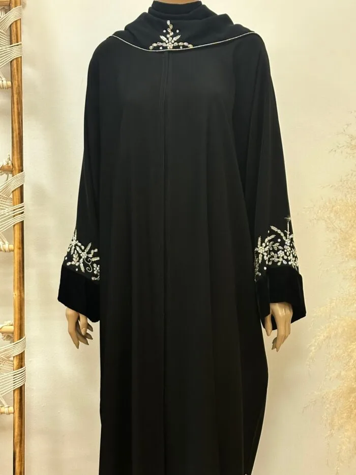 Elegant Serenadia Abaya featuring a luxurious Nida Premium fabric with intricate floral handwork and rich velvet accents. The abaya is complemented by a soft chiffon Sheila that drapes gracefully. The design blends traditional craftsmanship with contemporary sophistication, perfect for modern women who appreciate both beauty and comfort.