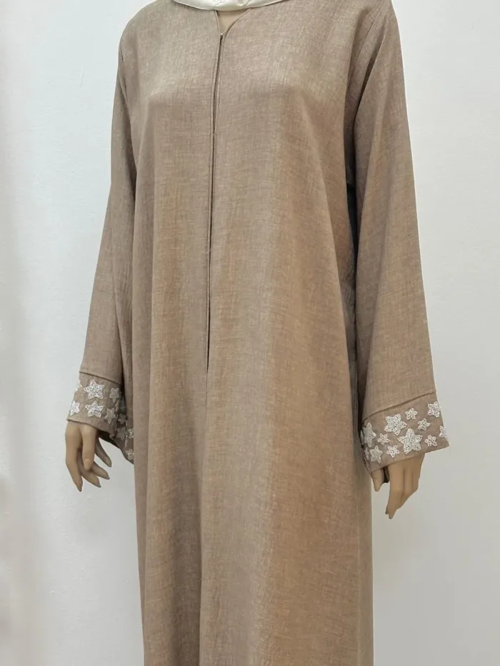 The Starlit Linen Abaya in soft, breathable linen features celestial star handwork on the sleeves and Sheila. The Sheila is crafted from airy chiffon, complementing the abaya’s elegant drape.