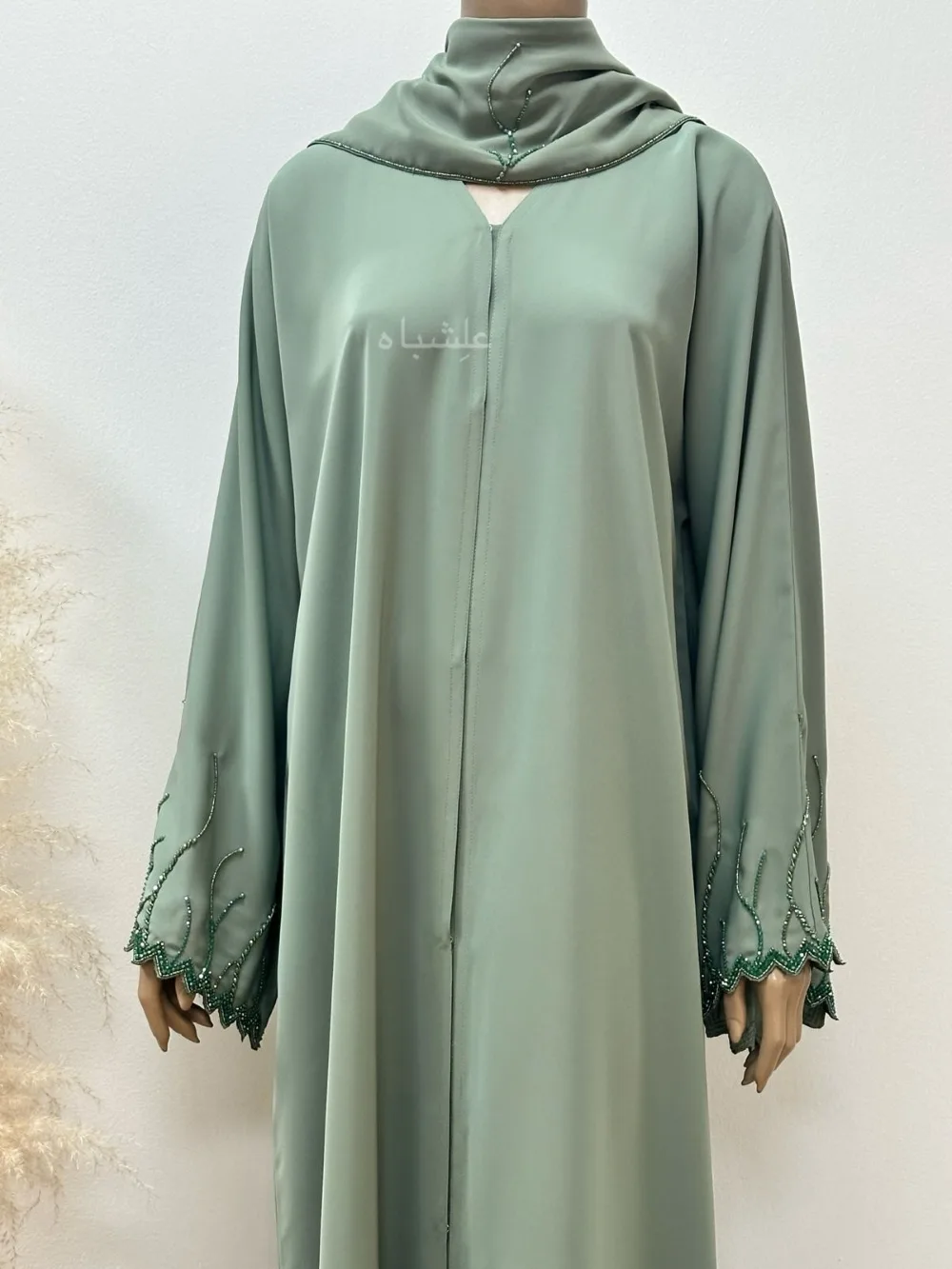 "Emerald Dawn Abaya by Alishbah featuring a vibrant emerald green color with zig-zag cut sleeves, adorned with dazzling crystals and beadwork. Accompanied by a matching sheila, the abaya combines modern design with timeless elegance, perfect for special occasions. The luxurious fabric and intricate embellishments create a sophisticated and radiant look."