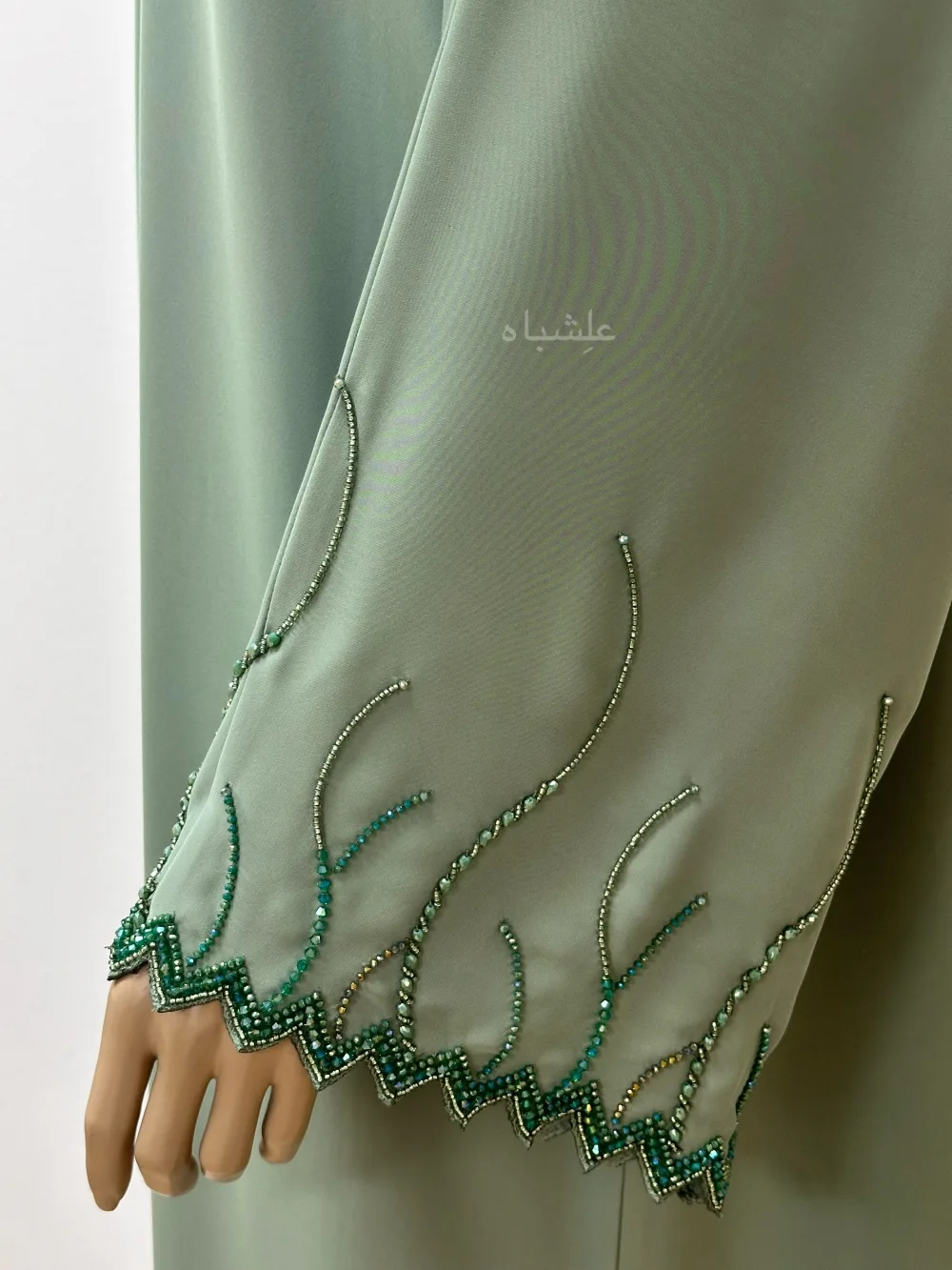 "Emerald Dawn Abaya by Alishbah featuring a vibrant emerald green color with zig-zag cut sleeves, adorned with dazzling crystals and beadwork. Accompanied by a matching sheila, the abaya combines modern design with timeless elegance, perfect for special occasions. The luxurious fabric and intricate embellishments create a sophisticated and radiant look."