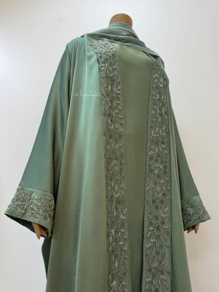 View from another angle Sage green abaya with intricate floral and leaf handwork along the front and cuffs, crafted from Khaleesi fabric, paired with a matching soft chiffon Sheila.