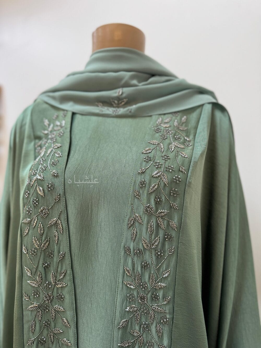 Top close up view of Sage green abaya with intricate floral and leaf handwork along the front and cuffs, crafted from Khaleesi fabric, paired with a matching soft chiffon Sheila.