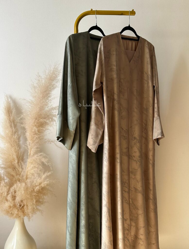 View of beige and green abaya hanging from a stand