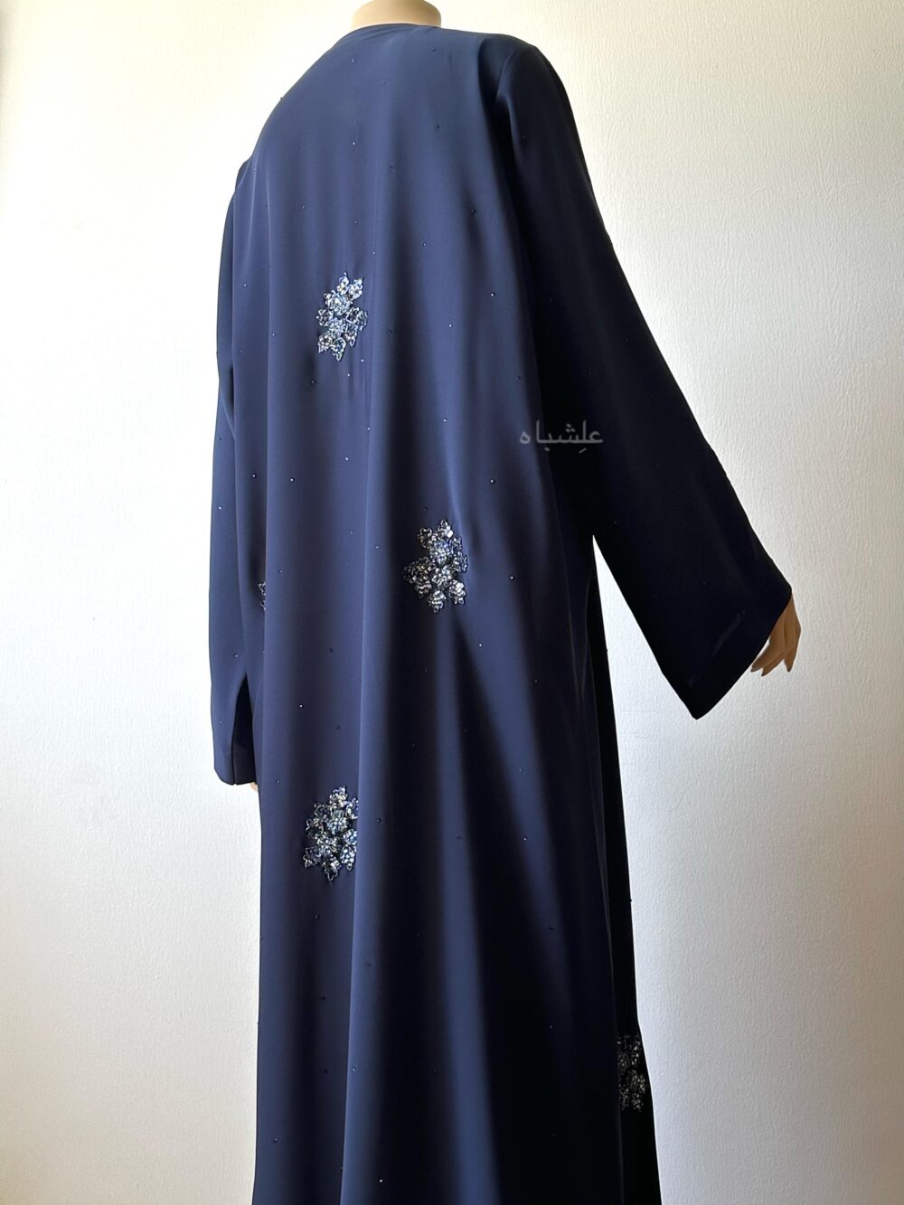 Back view of abaya showing the handwork and rhinestone work on back with one hand raised higher