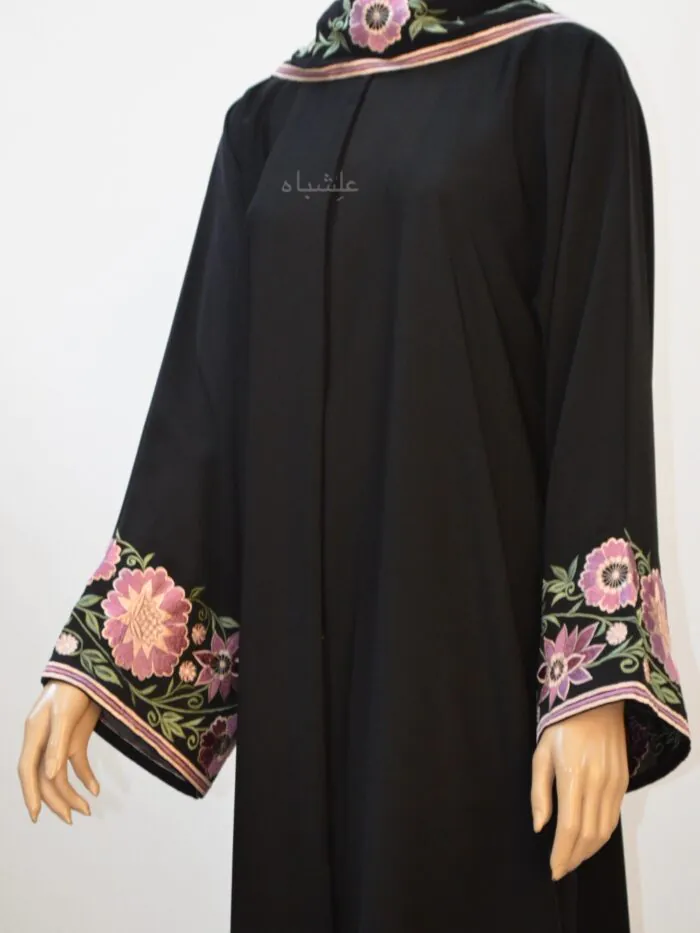 "Close-up image showcasing intricate floral embroidery in vibrant pink, purple, and white on the sleeves and sheila of a black abaya."