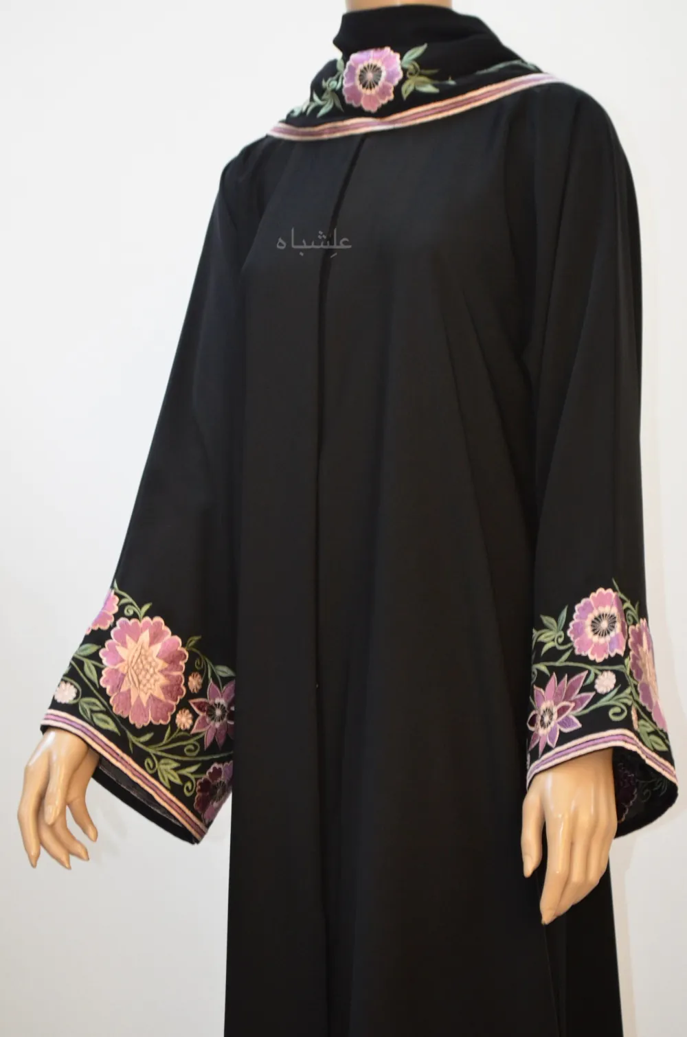 "Close-up image showcasing intricate floral embroidery in vibrant pink, purple, and white on the sleeves and sheila of a black abaya."