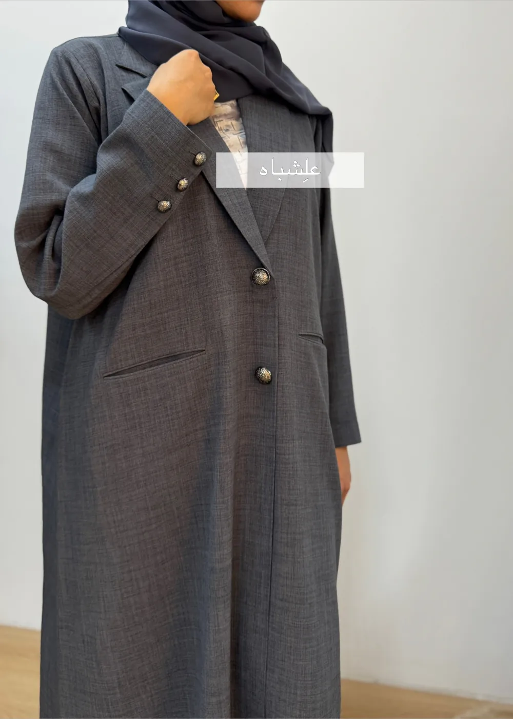 "Close-up of a woman wearing a black linen abaya by Alishbah, featuring elegant button details on the front and sleeves, paired with a soft chiffon Sheila."