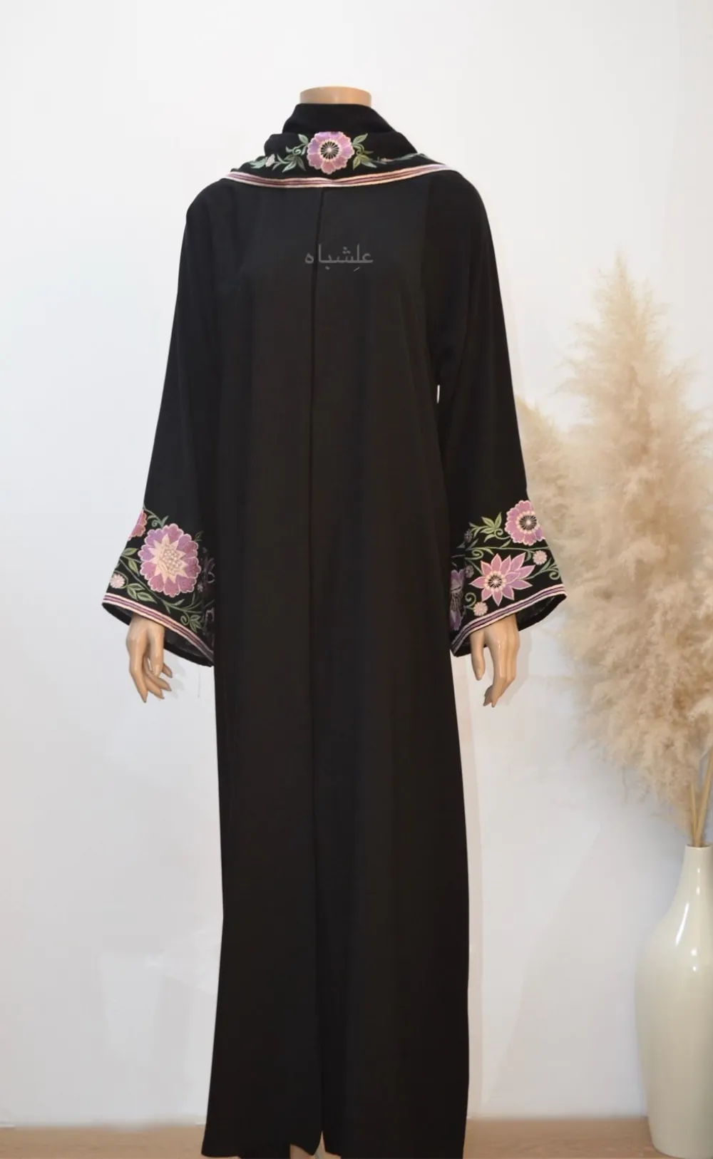 **Floral Elegance Abaya**: “Full-length image of the Floral Elegance Abaya featuring luxurious black Nida Premium fabric adorned with intricate floral embroidery in shades of pink, purple, and white on the sleeves and sheila. The abaya showcases a flattering, flowy silhouette and is complemented by a soft chiffon sheila with matching floral embroidery, embodying elegance and sophistication.”