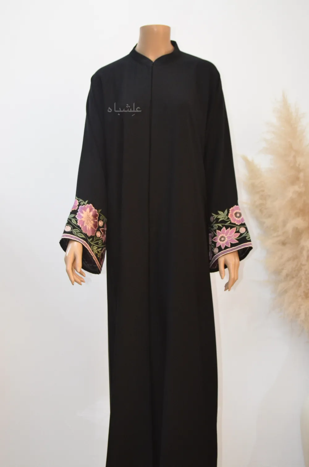 **Floral Elegance Abaya** without the sheila: “Full-length image of the Floral Elegance Abaya made from black Nida Premium fabric, featuring intricate floral embroidery in pink, purple, and white along the sleeves. The abaya is styled with a flattering, flowy silhouette and showcases the delicate floral details prominently on the sleeves, highlighting elegance and sophistication.”