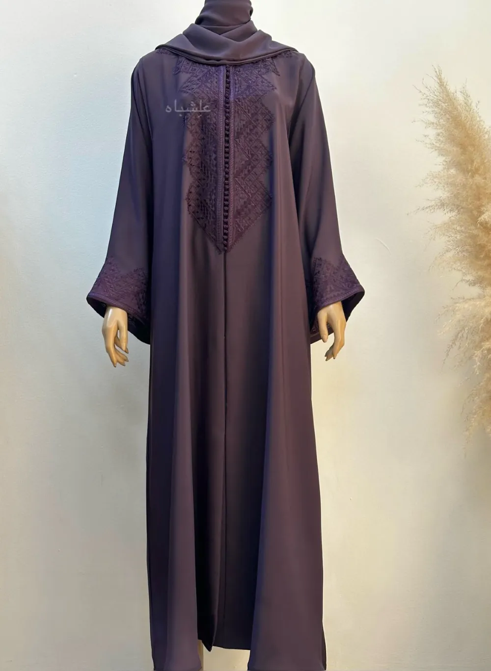 Full view of a A deep purple abaya made from Nida fabric featuring intricate geometric Magrabi hand embroidery along the front and sleeves, paired with a matching soft chiffon Sheila.