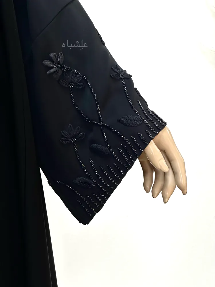 "Closeup of a woman’s hand wearing the Midnight Bloom abaya with matching chiffon sheila. The sleeve features intricate organza flower embroidery with fine threadwork details."