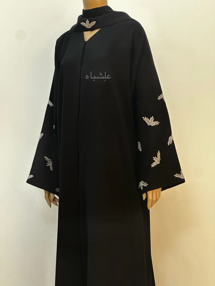 "Front view of the Leaf Whisper Abaya with sheila, displayed on a mannequin, showcasing black Ajwa Korea fabric and hand-embroidered leaf motifs."