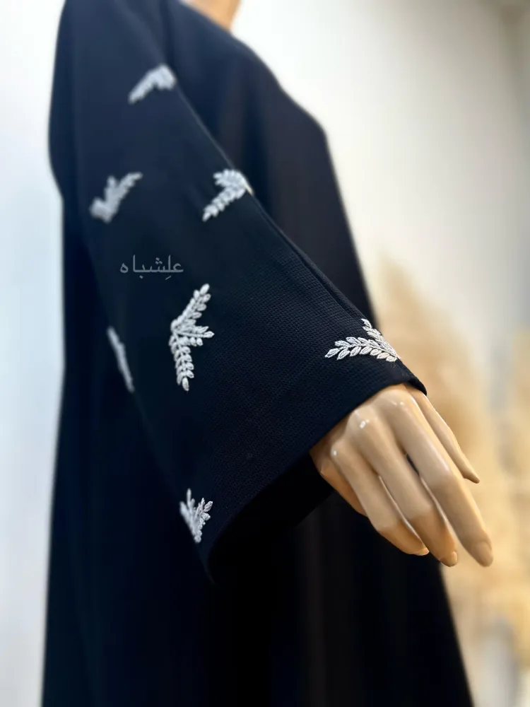 "Close-up of the Leaf Whisper Abaya’s hand-embroidered leaf motifs on the sleeves, with raised hands highlighting intricate detailing."