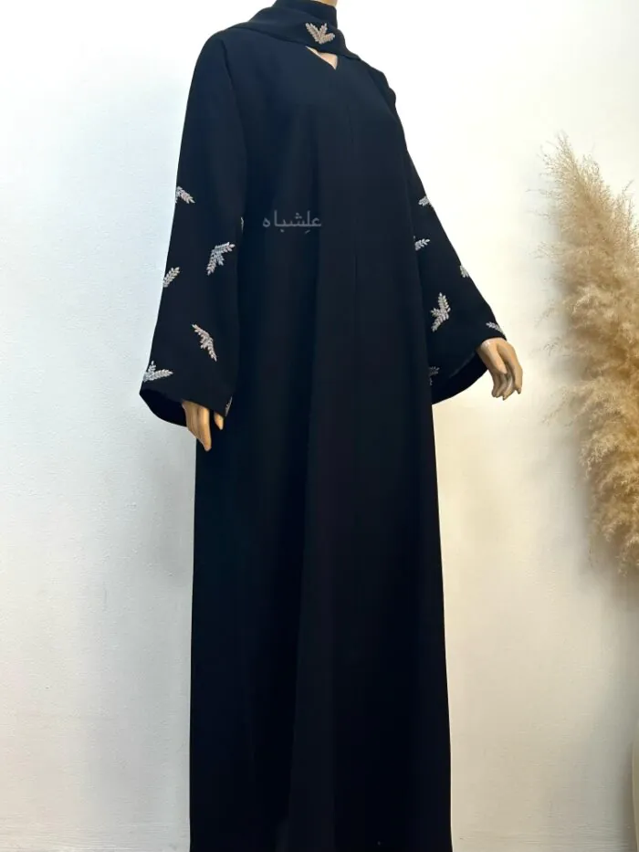 "Full view of the Leaf Whisper Abaya with sheila from a slight side angle, displayed on a mannequin, with one hand raised to highlight the embroidered sleeve detail."