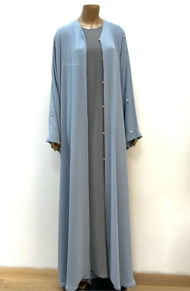 Front view shot of the abaya with the buttons open, revealing the inner abaya. The outer abaya, made from Egyptian Crape, showcases floral detailing on the sleeves.